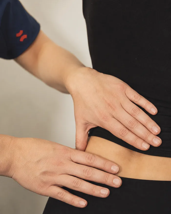 Las manos de una kinesióloga de Spark Wellness evalúan la zona lumbopélvica de una paciente